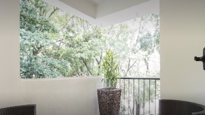 Ein Balkon mit Korbmöbeln, einer Topfpflanze und Blick auf Bäume.