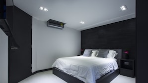 Ein modernes Schlafzimmer mit einem Bett, das auf einer Plattform zentriert ist, einer dunklen Akzentwand, einem kleinen Nachttisch mit einer Vase und Einbaustrahler.