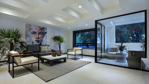 Ein modernes Wohnzimmer mit einer Couch, einem Couchtisch und Sesseln, einem großen Gemälde und Blick durch eine Glastür.