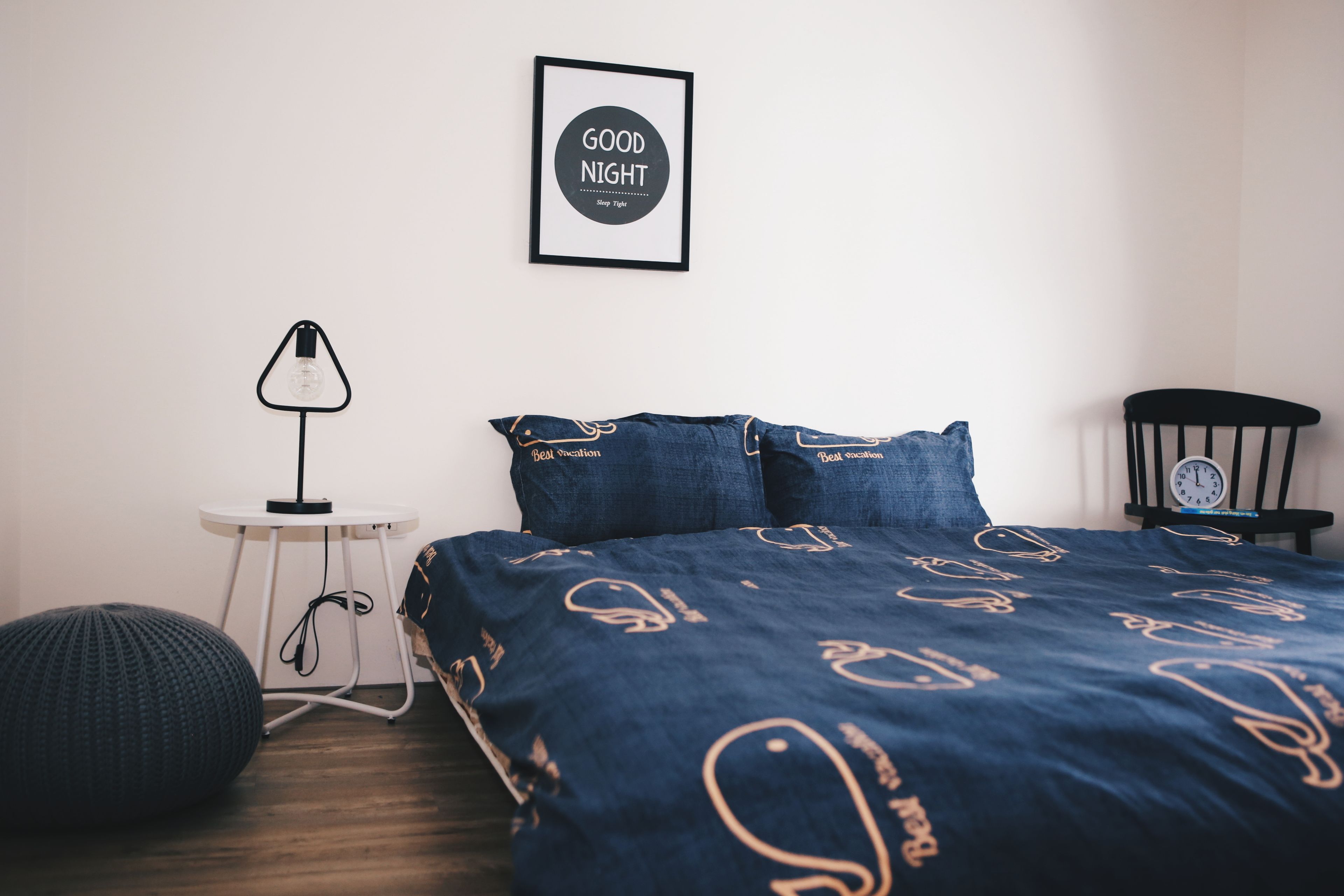 Une chambre à coucher avec un lit, une table de chevet, une lampe, une horloge et un mur orné d’un tableau.