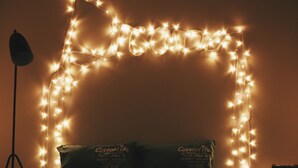 Ein Bett mit zwei Kissen, eine Stehlampe und Lichterketten, die eine Herzform an der Wand bilden.