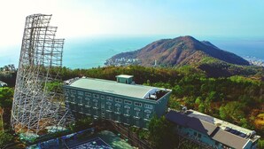 A hotel with a tennis court, a large metal structure, and a mountain in the background. - Ho May Resort (Ho Chi Minh City)