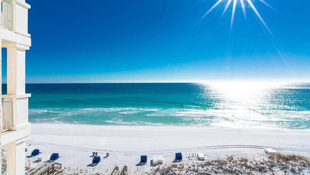 A beach view from a balcony with sun shining over the ocean, a sandy beach, and several lounge chairs. - Inn at Crystal Beach 608b * Gulf Front with Beach Chair Set. Onsite dining! (Destin)