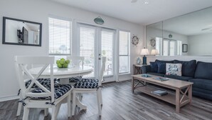 A modern living room with a white dining table, two white chairs, a wooden coffee table, a dark blue sofa, and a large mirror.
