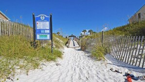A sandy beach path with a 'Safety First' sign, a wooden fence, and scattered beach shoes.