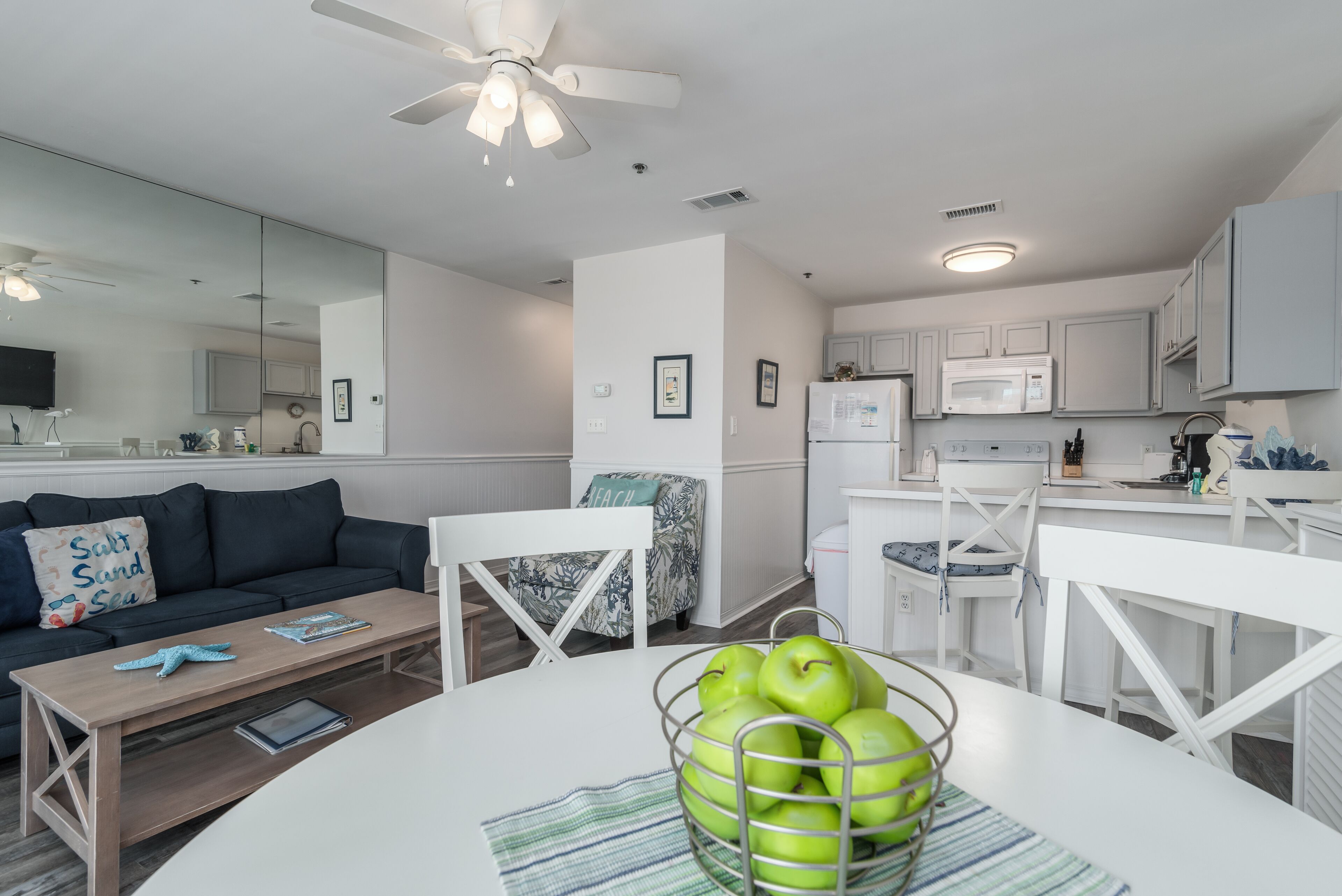 Una sala de estar moderna con sofá, mesa de centro y mesa de comedor con frutero.
