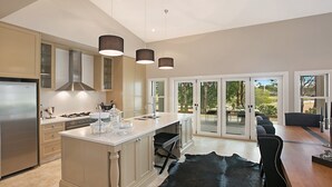 Une cuisine moderne dotée d’un îlot central, d’appareils électroménagers en acier inoxydable et de luminaires suspendus.