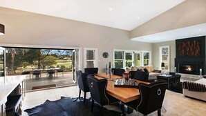 Un vaste espace de vie comprenant une grande table à manger, des chaises à revêtement noir, une cheminée et une vue sur l’extérieur.