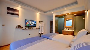 Ein Hotelzimmer mit zwei Betten, einem Fernseher, einem Spiegel, einem Waschbecken und einem Regal mit einem Wasserkocher.