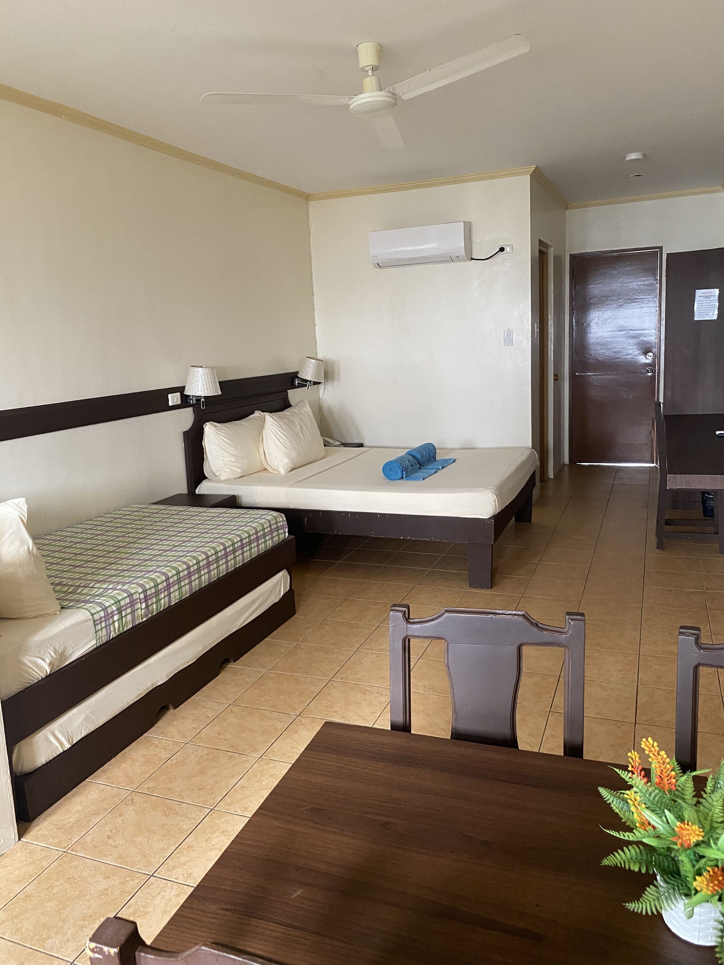 A hotel room with a bed, a desk, a chair, and a ceiling fan.