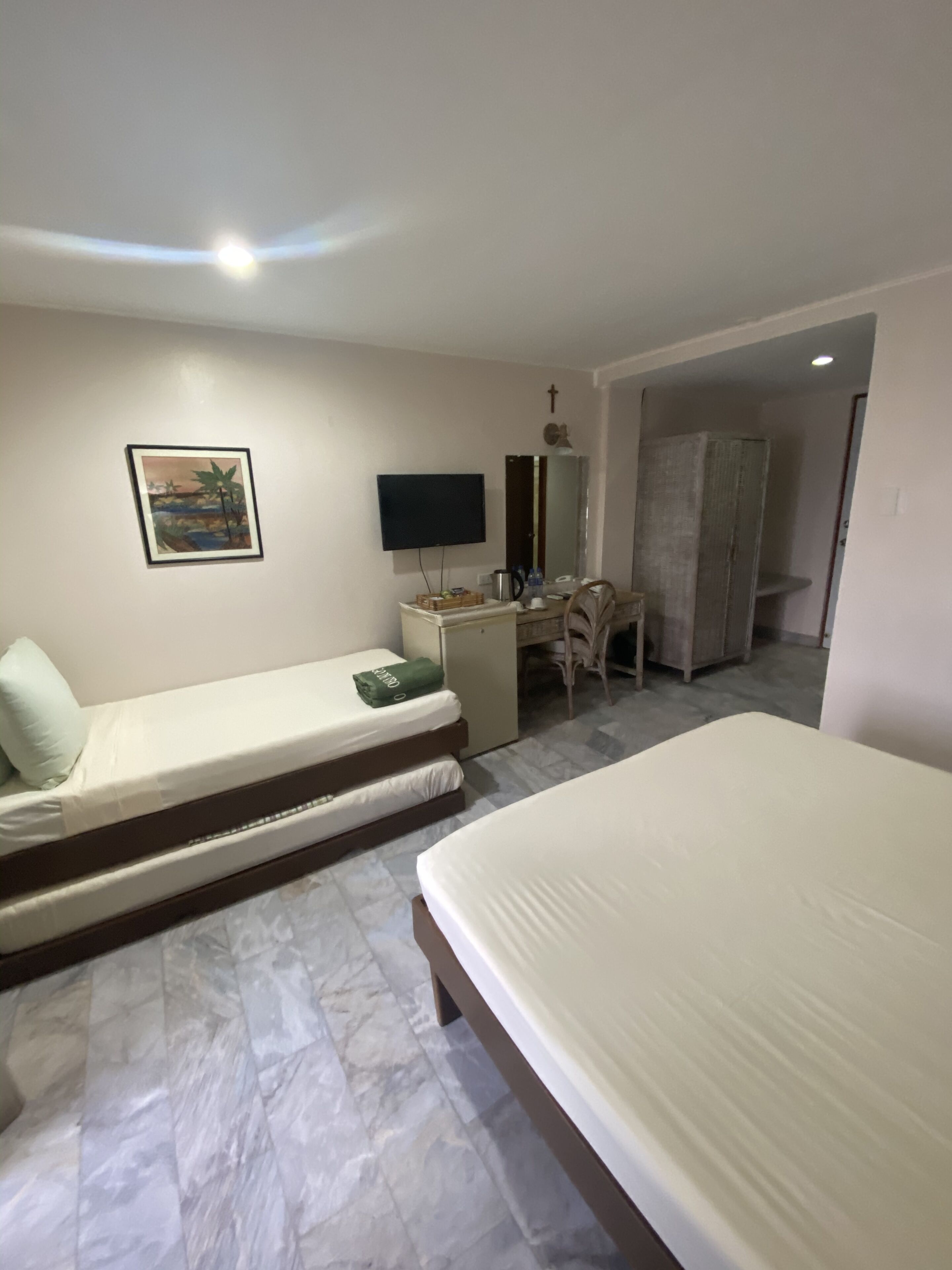 A hotel room with two beds, a desk, a chair, a television, and a wardrobe.