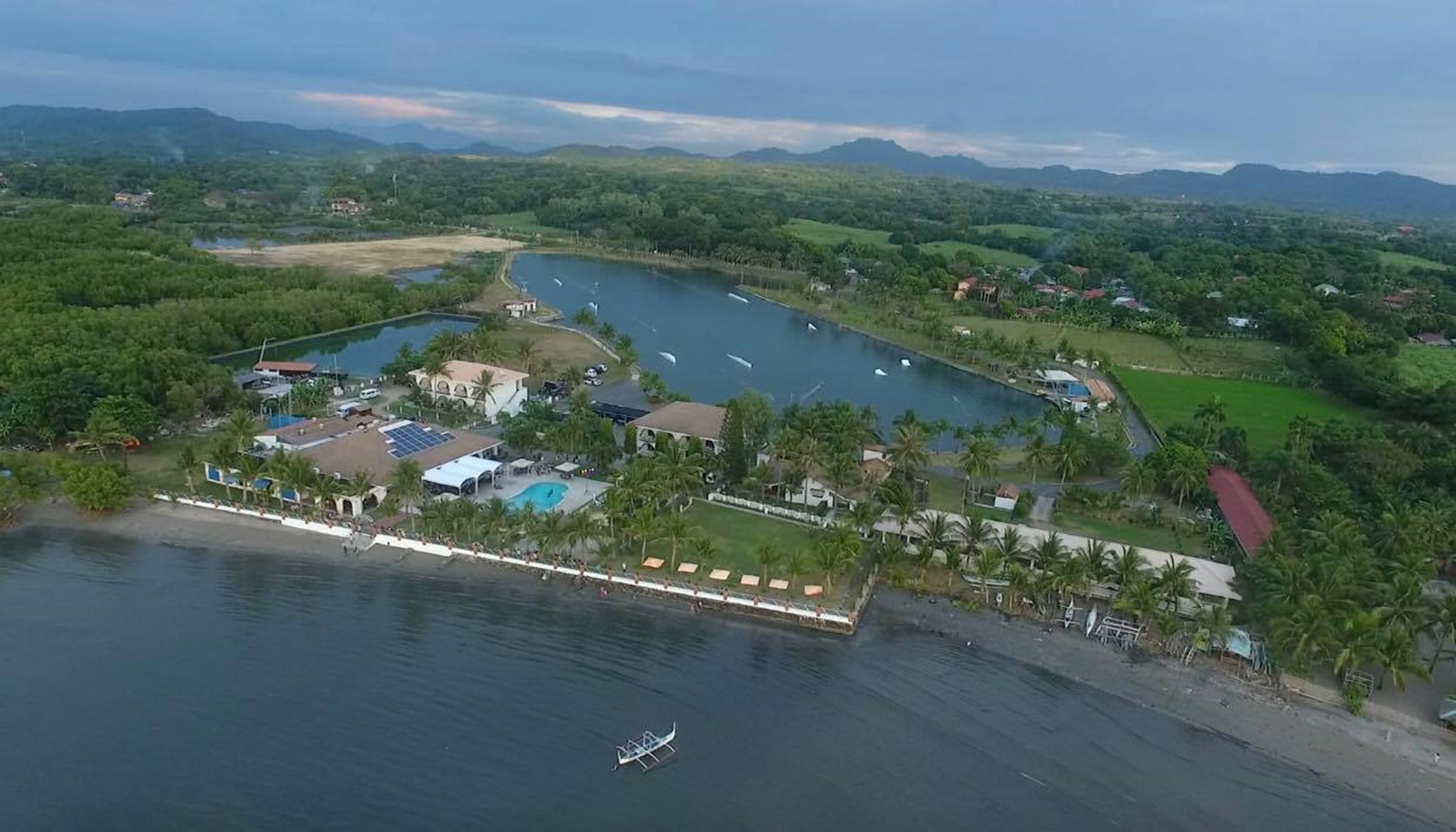 An aerial view of a coastal resort with a marina, swimming pools, and lush greenery.