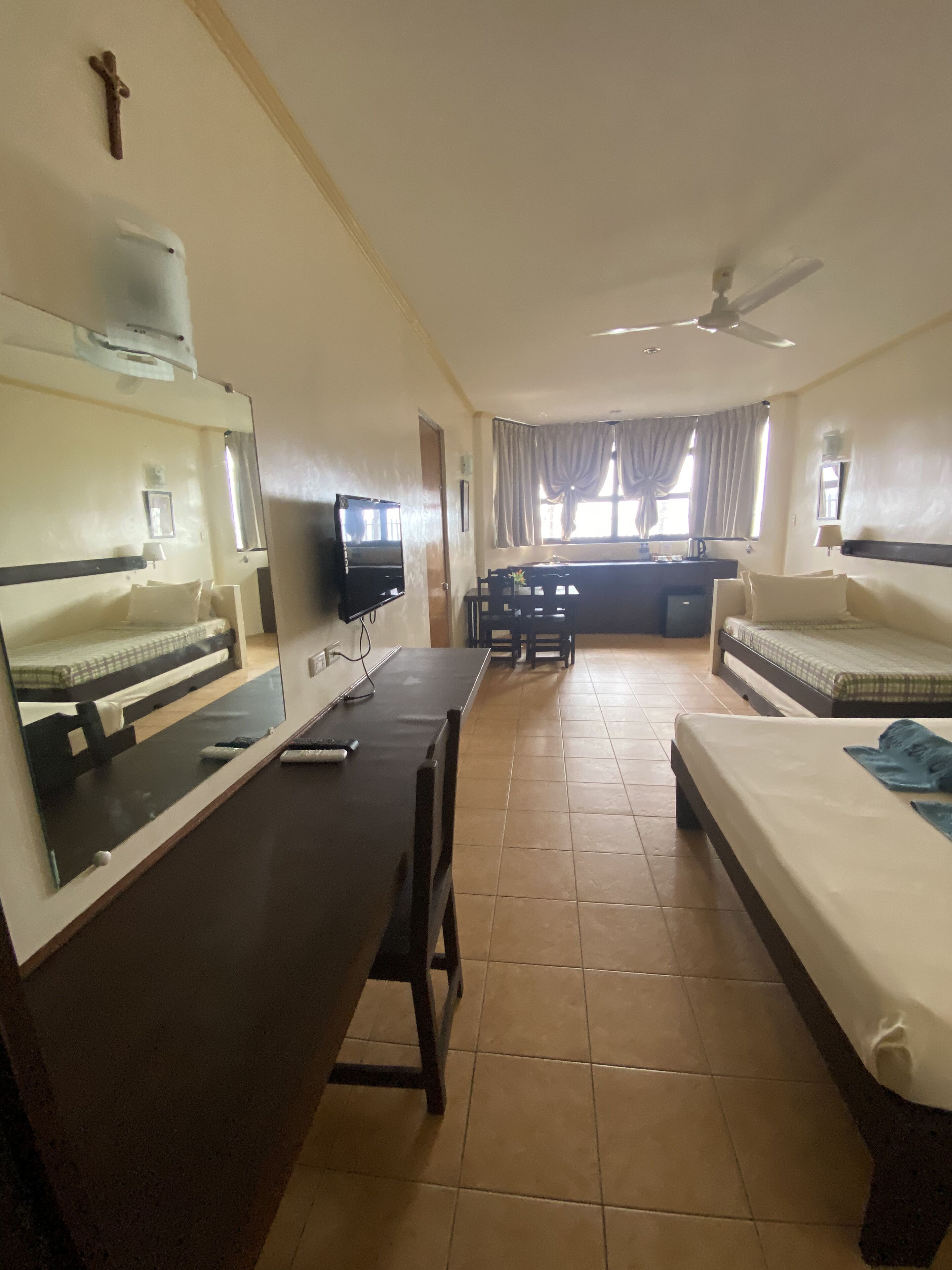 A hotel room with a bed, a desk with a TV, a dining area with a table and chairs, and a ceiling fan.