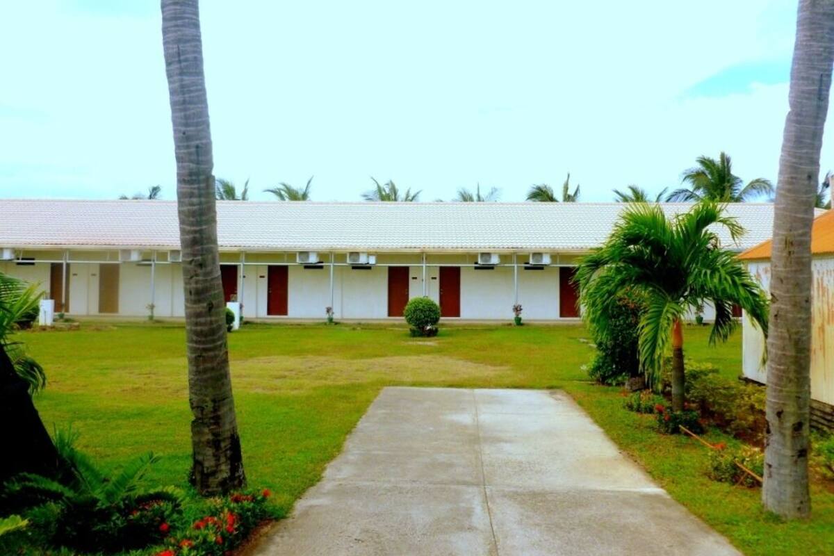 A row of single-story motel rooms with a central courtyard, palm trees, and a concrete walkway.