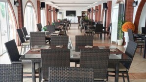 Un comedor amplio con varias mesas y sillas, que presenta un diseño moderno con detalles de ladrillo y grandes ventanales.