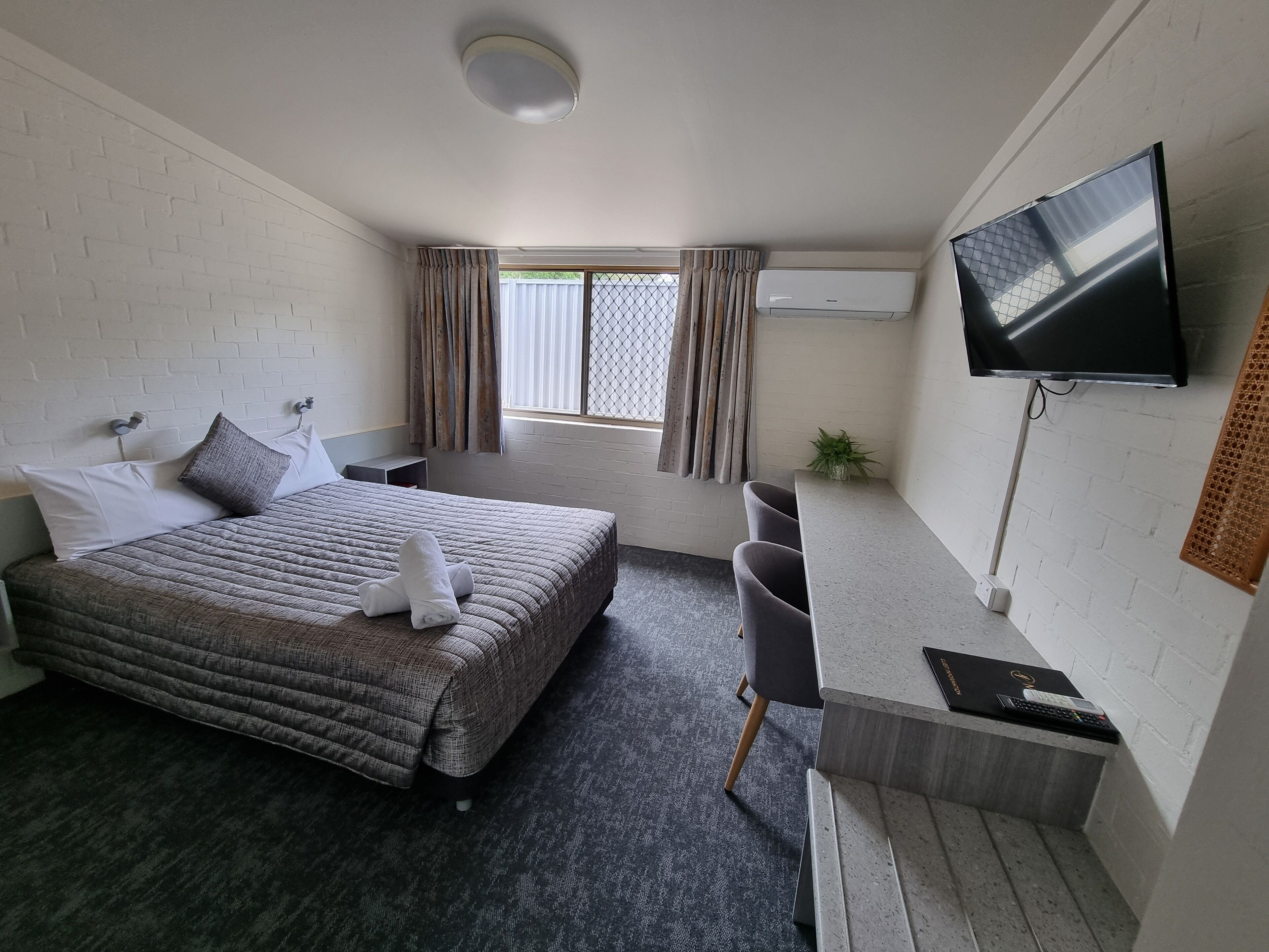 A hotel room with a bed, a desk, a TV, and a window with curtains.