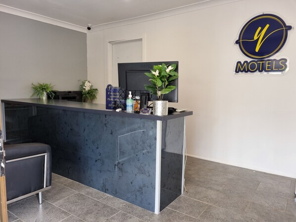 A reception desk with a modern design, a potted plant, a sign for reception, and a logo for 'MOTELS'.