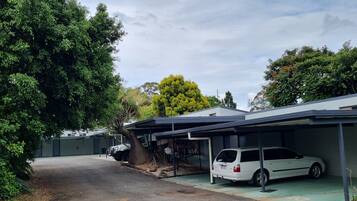 A parking area with two white vans parked under a covered structure, surrounded by greenery and trees.