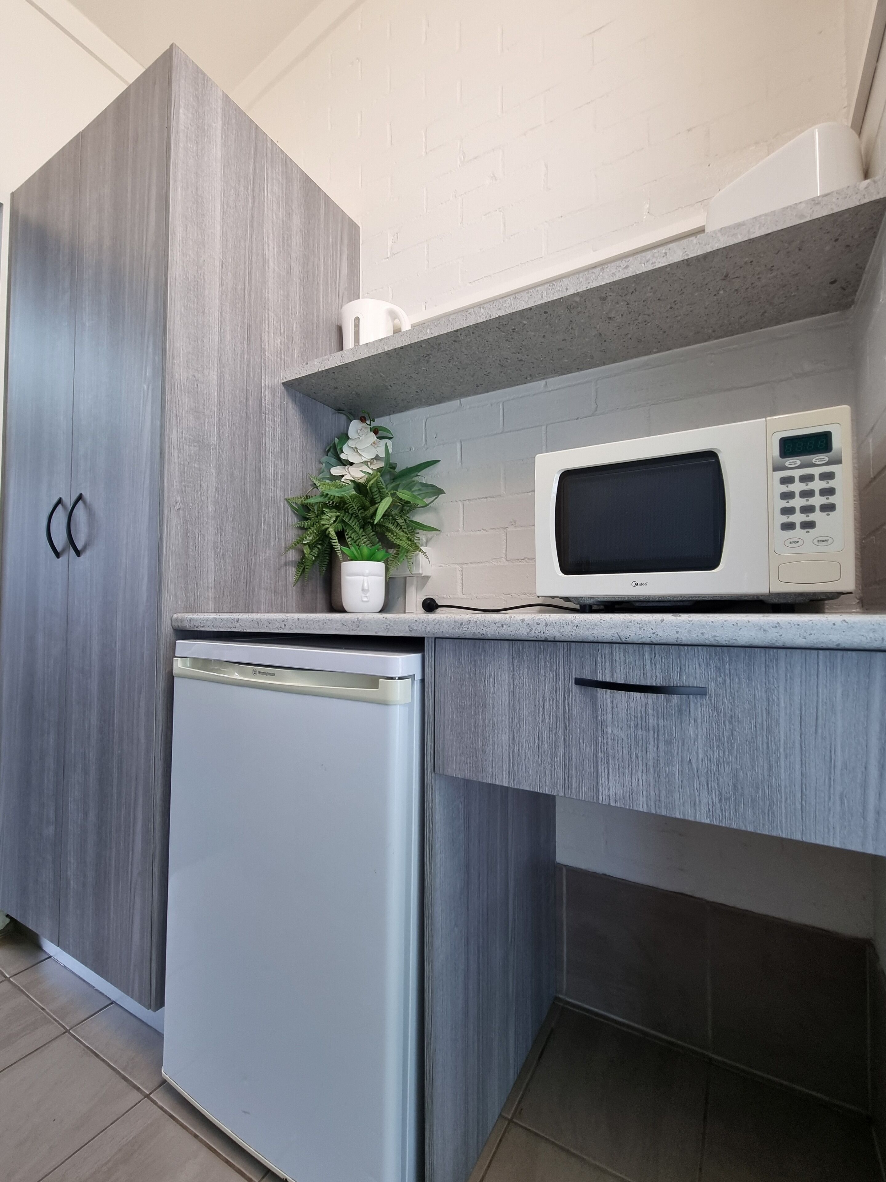 A compact kitchen with a built-in microwave, a small refrigerator, and a potted plant on the counter.