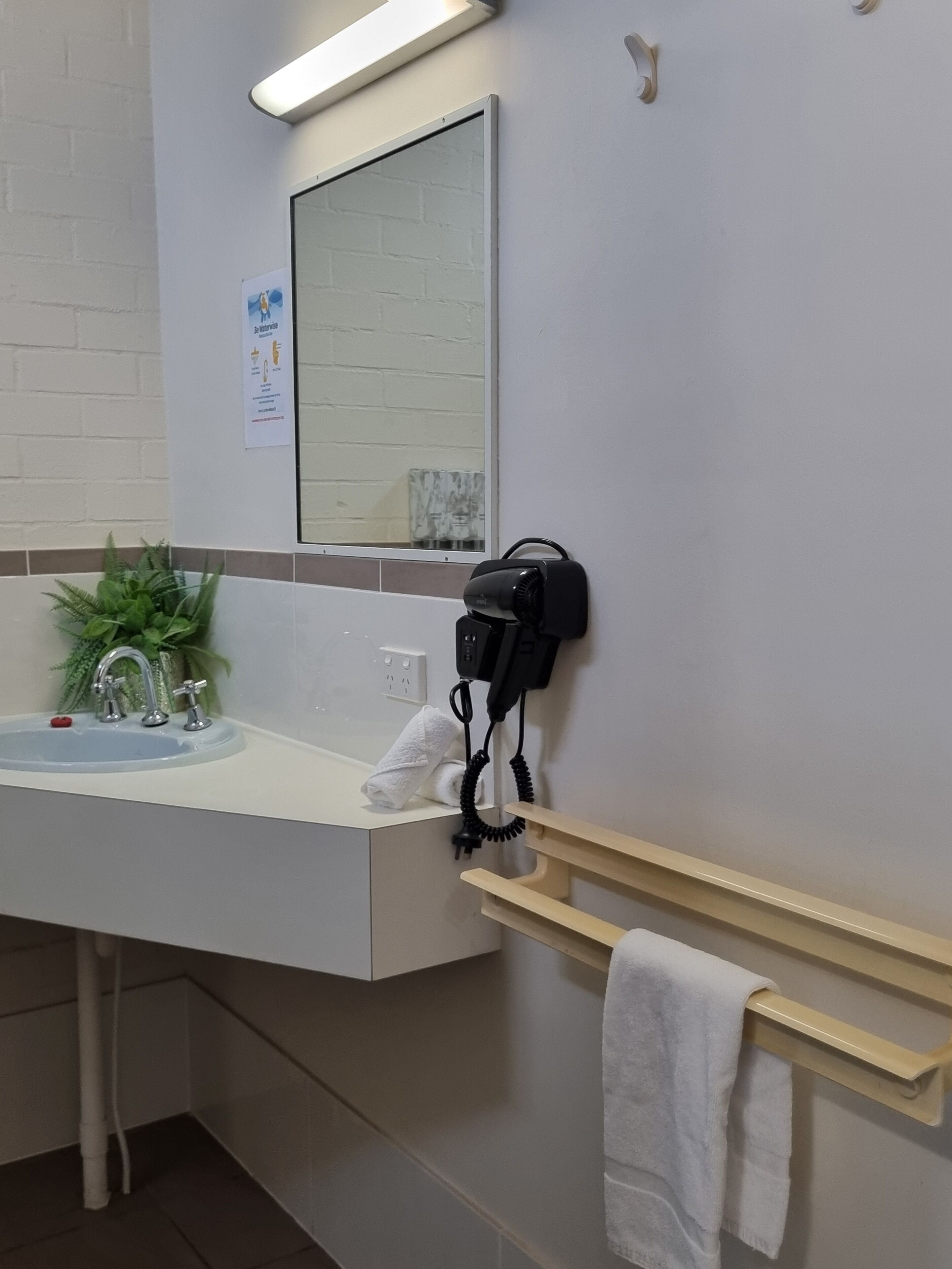 Un baño moderno con un lavamanos blanco, un espejo, un secador de pelo y un perchero para toallas.