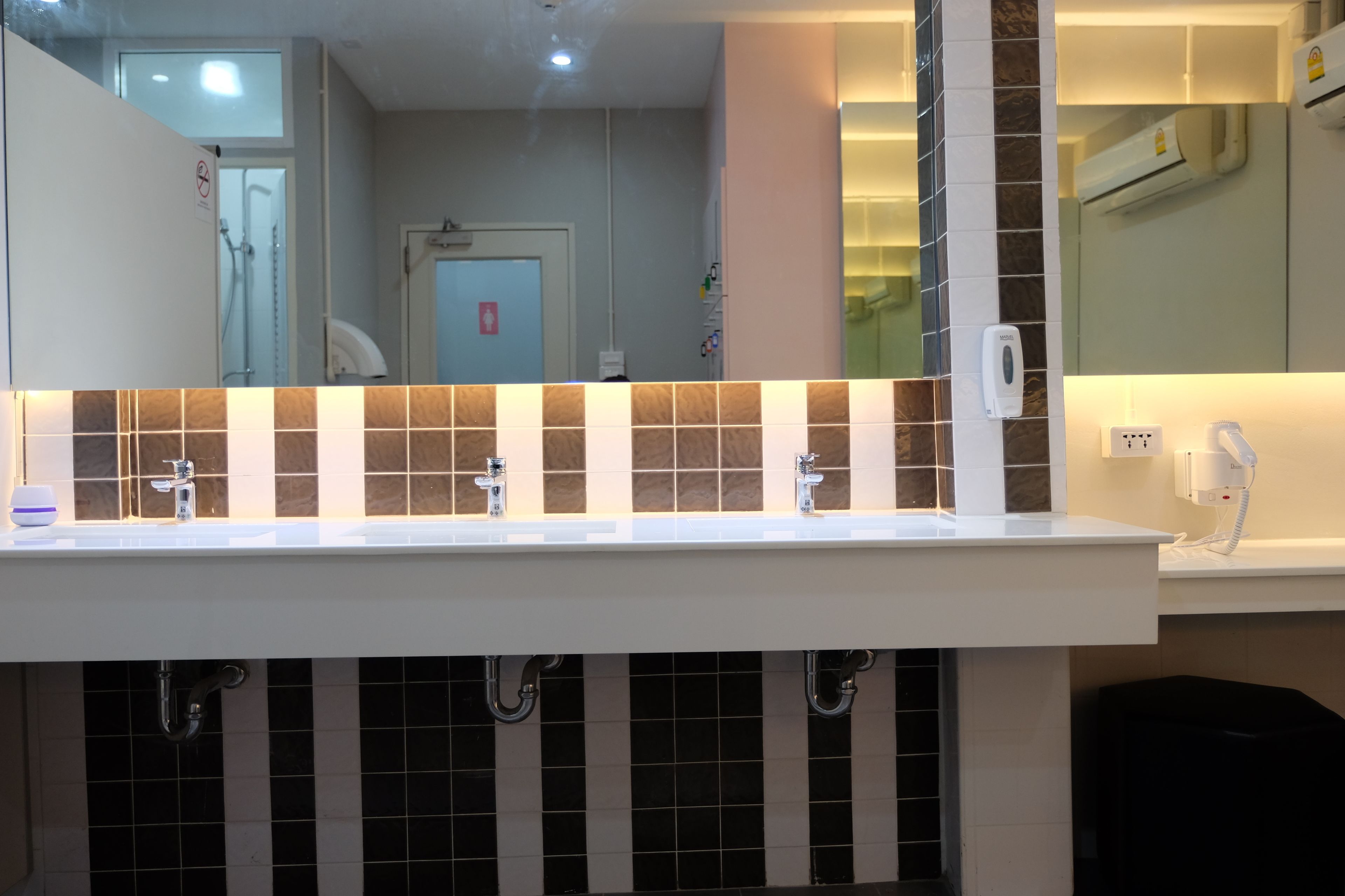A modern bathroom with a white sink, black and beige tiles, and a mirror.