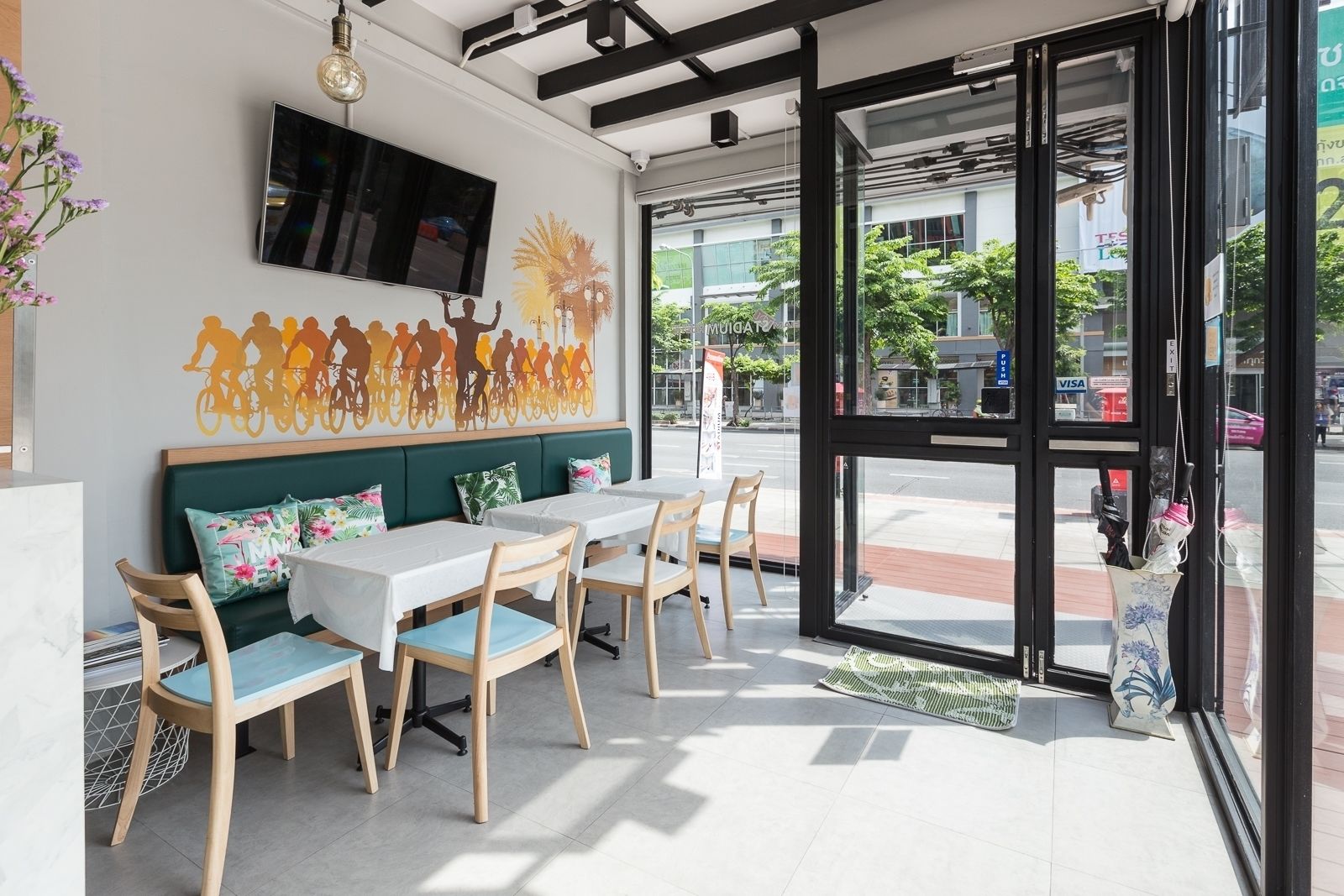 Un café moderno con una zona de estar que incluye mesas y sillas, un sofá con cojines, un televisor de pantalla plana en la pared y vistas a la calle.