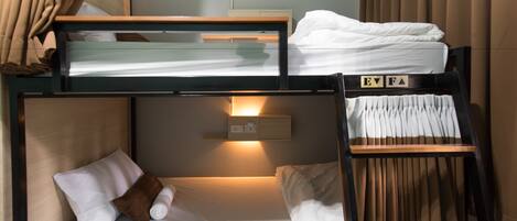 A bunk bed with a wooden ladder, a bedside table with a lamp, and a wall-mounted power outlet.
