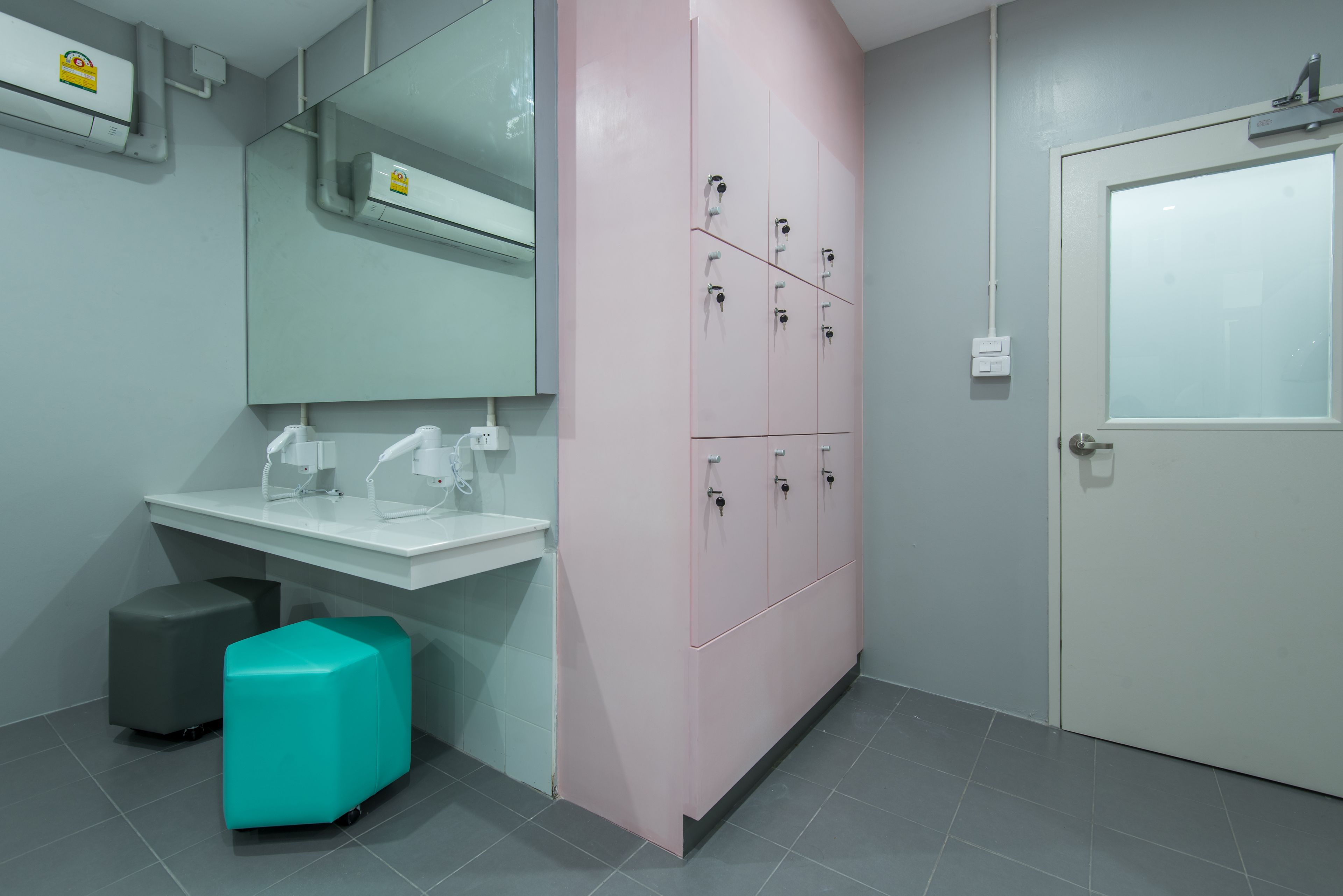 Un baño con lavamanos blanco, espejo, mueble rosa y puerta blanca.