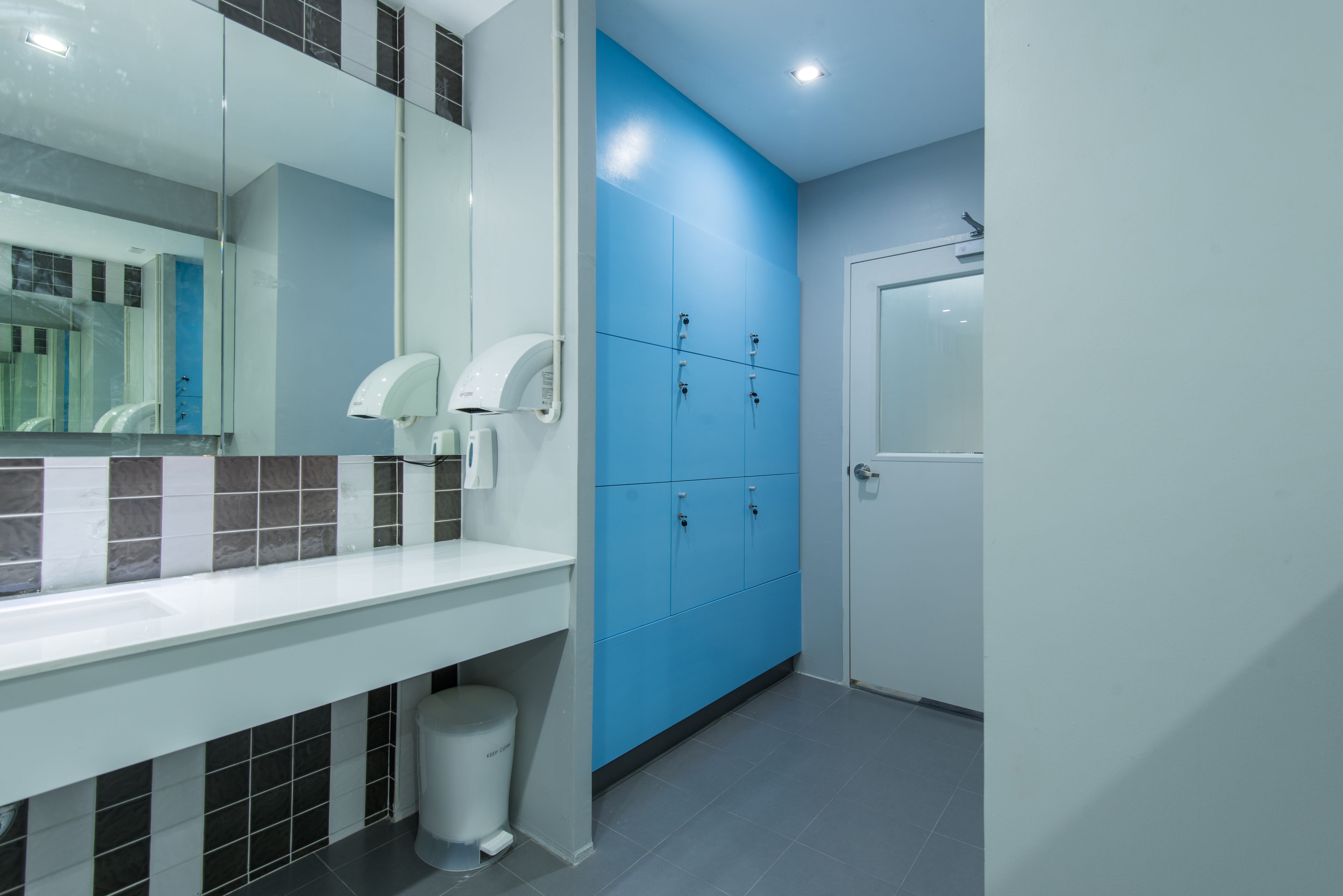 A modern bathroom with a white sink, blue lockers, and a white trash bin.
