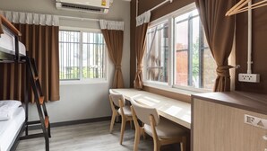 Ein kleines Zimmer mit einem Etagenbett, einem Schreibtisch mit Stühlen, einem Fenster mit Vorhängen und einer Steckdose.
