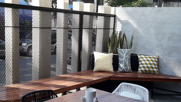 A wooden bench with cushions and a white chair, a small table with a white mug, and a potted plant. - APARTMENT IN THE HEART MIRAFLORES (Miraflores)
