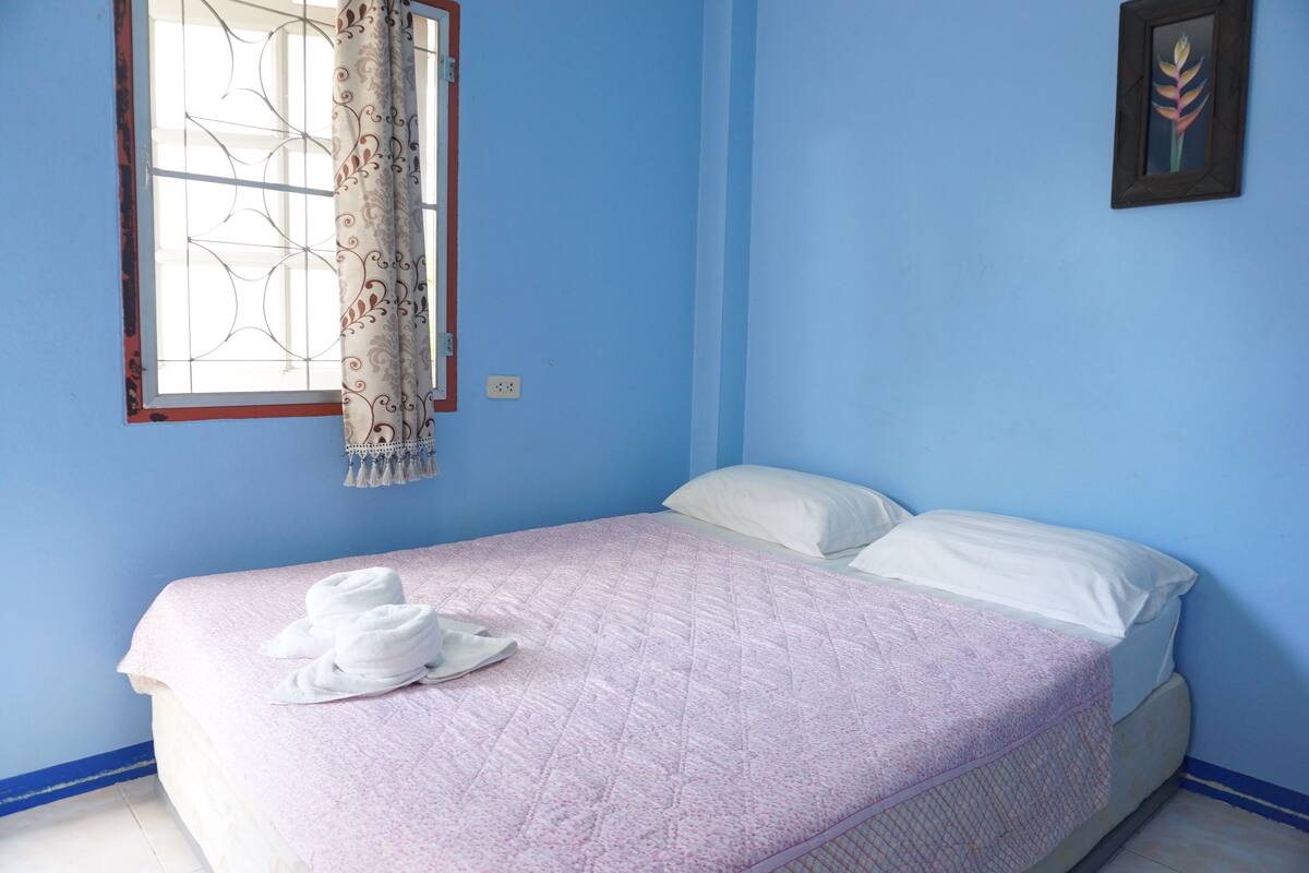 A bedroom with a single bed, a window with decorative curtains, and a wall-mounted picture.