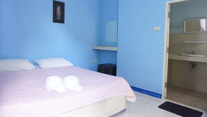 A bedroom with a bed, pillows, a bedside table, a mirror, and a bathroom with a sink and toilet. - Dahla House Ranong (Ranong)