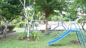 A playground with a slide and swings in a grassy area with trees. - Dahla House Ranong (Ranong)