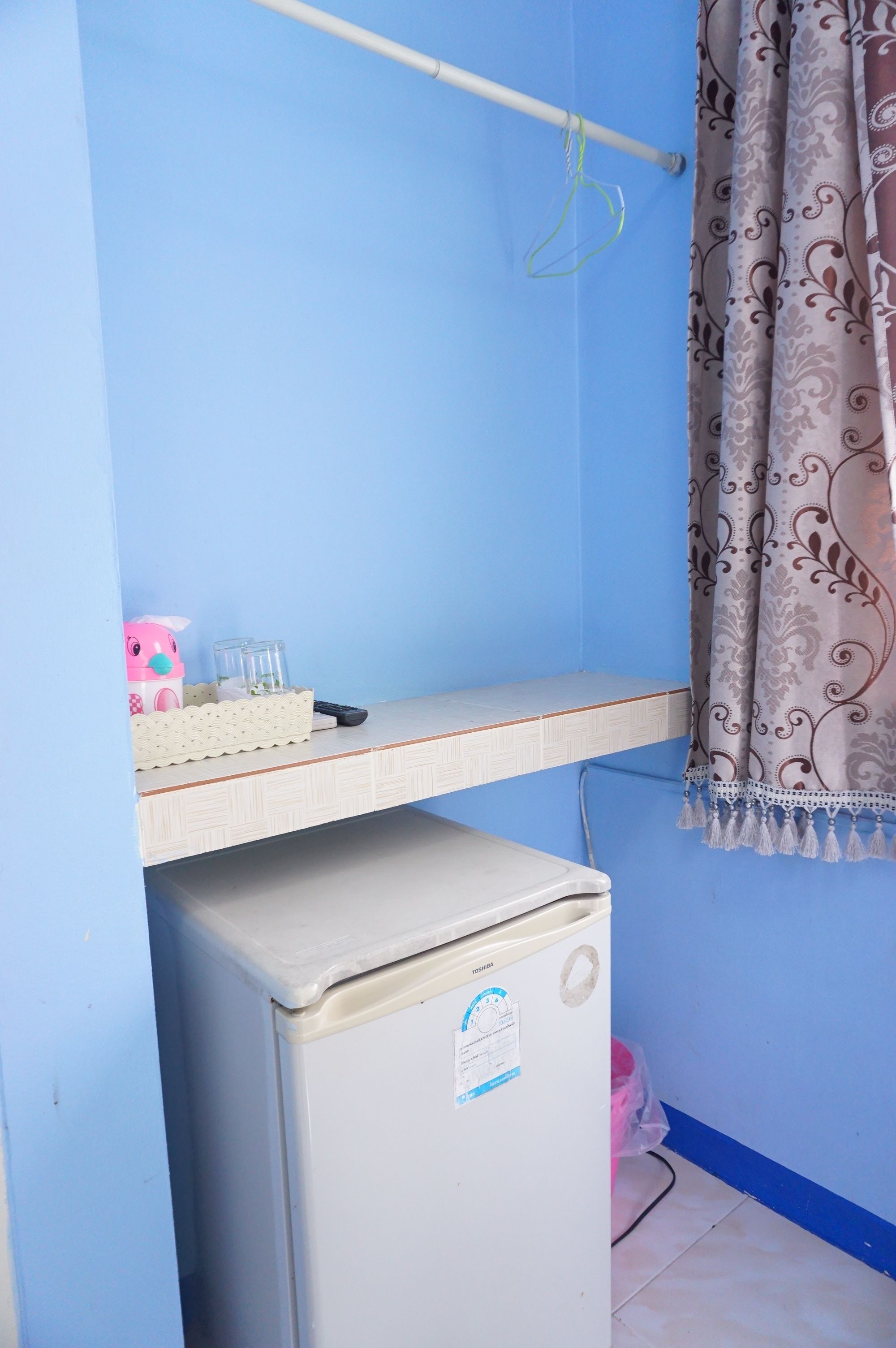 Una habitación pequeña con pared azul, un escritorio blanco con tendedero colgante, un juguete rosa y un refrigerador.