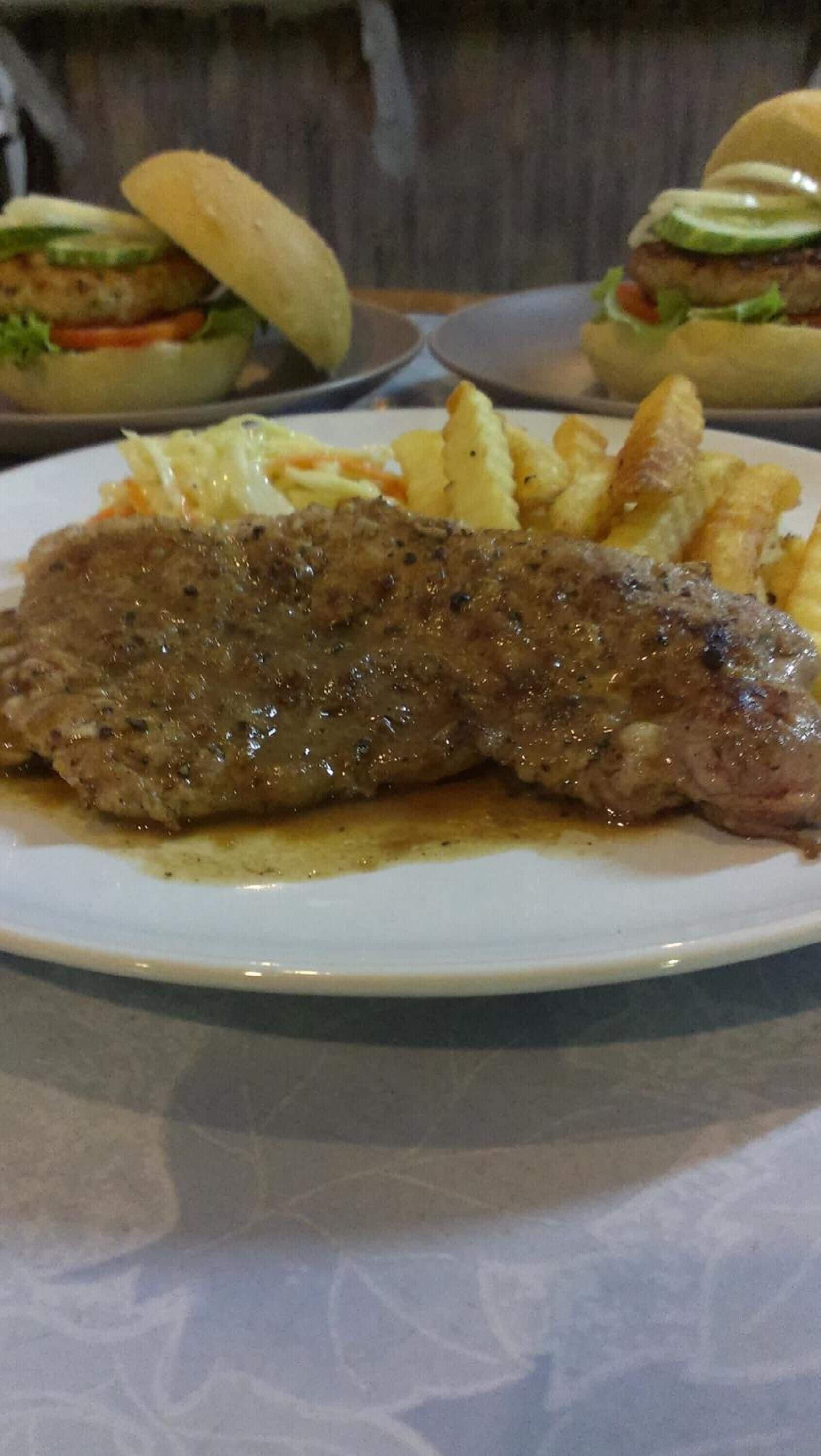 Une assiette contenant un plat de viande grillée, peut-être un steak, accompagné d’une portion de frites et d’une salade.