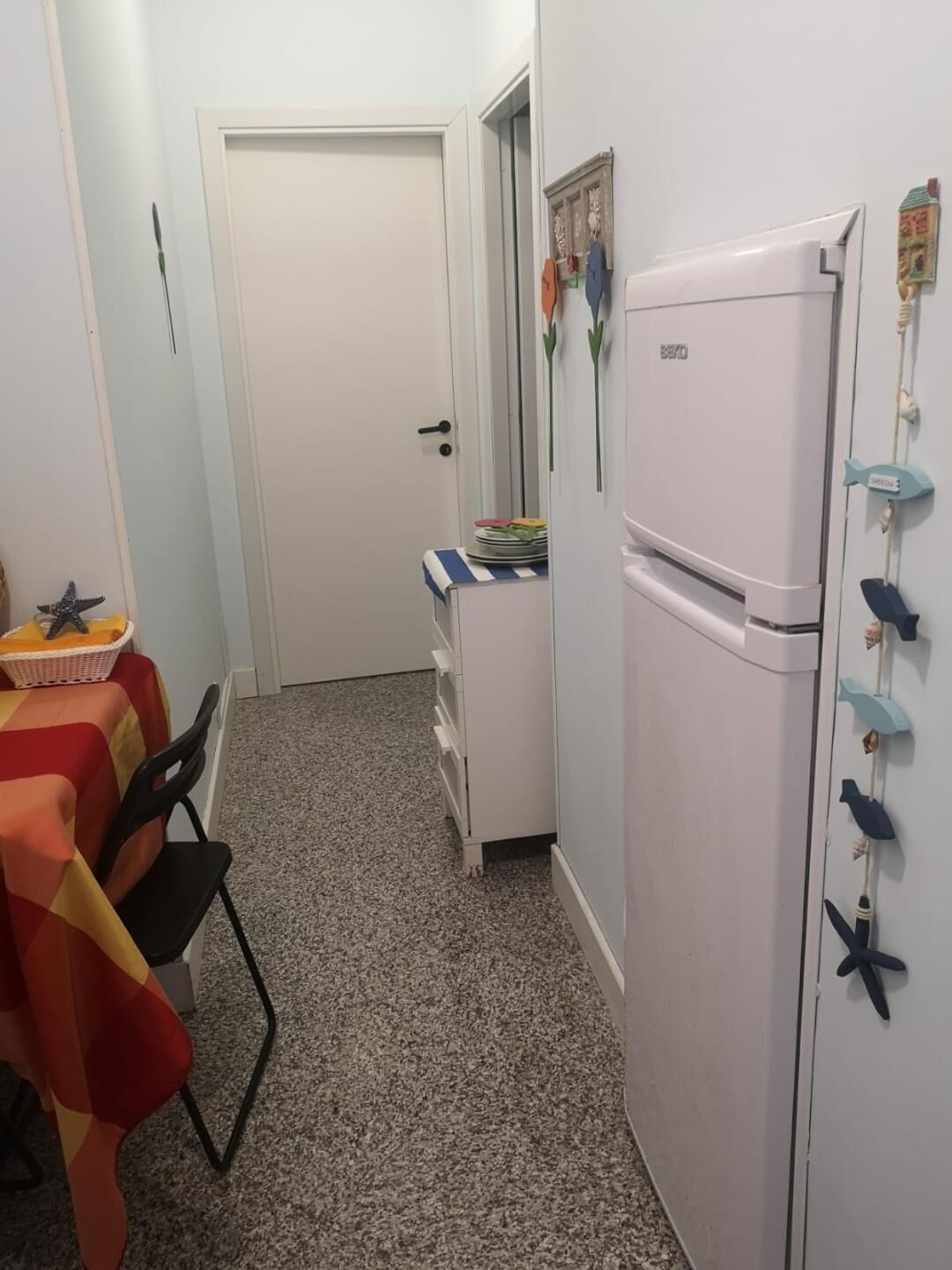 A compact kitchen with a white refrigerator, a small table with chairs, and a door leading to another room.