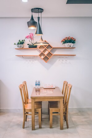 A dining area with a wooden table and chairs, pendant lights, and wall-mounted shelves with plants and glasses. - Blue Ocean Apartment (Nha Trang)