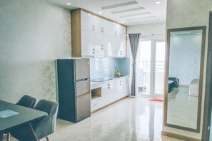 A modern kitchen with white cabinets, a refrigerator, and a dining area with a table and chairs. - Blue Ocean Apartment (Nha Trang)
