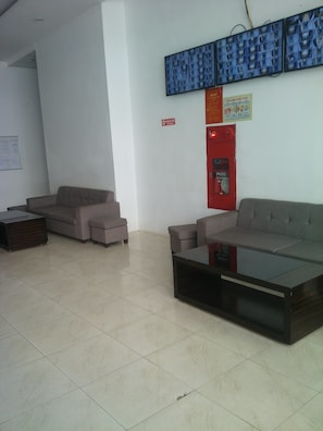 A modern waiting area with sofas and a coffee table, a fire extinguisher, and a wall-mounted display.