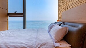 Een slaapkamer met een groot raam, een bed met witte beddengoed en een houten hoofdeinde.