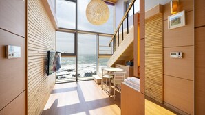 Een modern interieur met een groot raam met uitzicht op de zee, houten lambrisering, een eethoek en een trap.