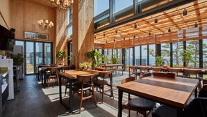 Een ruime restaurantruimte met houten inrichting, grote ramen en uitzicht op de zee.