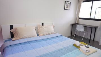Una cama bien hecha con una colcha azul y blanca a cuadros, dos almohadas y una toalla doblada al lado.