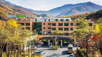 Un hotel moderno con una entrada central, rodeado de follaje otoñal y montañas al fondo.