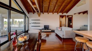 Een moderne woonkamer met een houten plafond, een eethoek met een tafel gedekt voor twee personen, een bank en een televisie.