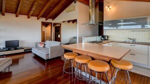 Een moderne woonkamer met een houten plafond, een keuken met witte tegels en een groot eiland met krukken.
