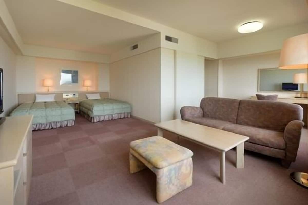 A hotel room with two beds, a sofa, a coffee table, a TV, and a lamp.