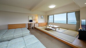 A hotel room with two beds, a desk, a chair, a small table, and a large window offering a view.