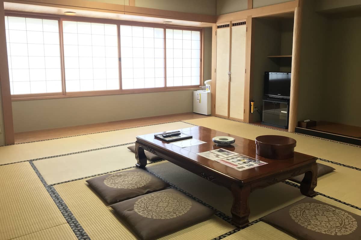 A traditional Japanese room with tatami flooring, a low wooden table, cushions, sliding doors, and a television.